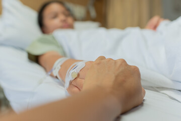 Obraz na płótnie Canvas Young patient asian woman lying on bed, focus hand holding hand of sick kid and mother on bed were connected to saline solution in hospital. Selective focus, healthcare and health insurance concept.