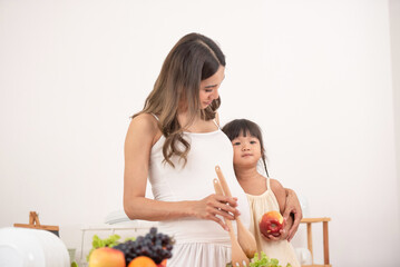 Mom with her two children eating fruits and vegetables. Mother with daughter having breakfast at home. Happy lifestyle family. Mother with her children in the kitchen cooking together.