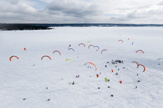 Aerial view of snowkiting competitions with colored parachutes on a frozen river covered with snow in winter