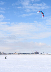 Snowkiting with colored parachute on a frozen river covered with snow in winter, with a city on the horizon