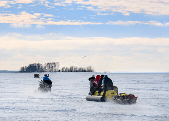 Fototapeta na wymiar Tourists on a snowmobile with inflatable sleds rush in the snow dust on a frozen river