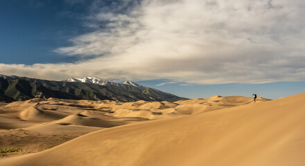 Fototapeta na wymiar Hiker Walking Down The Steep Edge of Sand Dune