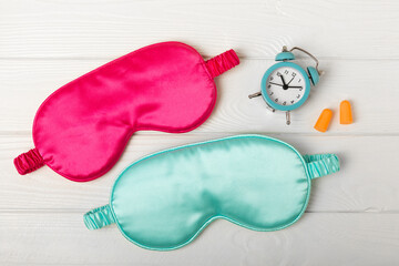Sleep mask, alarm clock, earplugs and sleeping pills on a white texture background.Top...