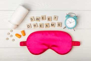 Sleep mask, alarm clock, earplugs and sleeping pills on a white texture background.Top...