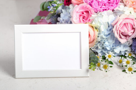 Horizontal white photo frame with flower bouquet on marble table