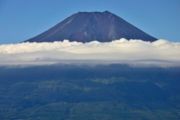 道志山塊の杓子山山頂より望む夏の富士山
杓子山は道志山塊の西に聳える山。富士吉田市と都留市、そして忍野村との行政界に位置する山。遠方から杓子山方面を眺めると富士山に近いこともありすぐにそれと分かるが、そのときに最も標高が高い山容は鹿留山或いは子ノ神であり、その隣のやや低い場所の山が杓子山になる。山梨百名山である杓子山の山頂からは、天候に恵まれれば四囲に視界を遮る樹木はほとんどないことから360度の