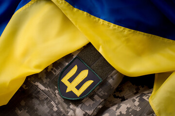 Yellow-blue flag of the state of Ukraine over military pixel camouflage fabric and chevron...