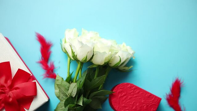 Bouquet of white roses with red bow on blue background. Boxed gift on side