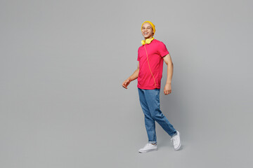 Full body side view smiling happy fun cheerful young man of African American ethnicity 20s wear pink t-shirt yellow hat headphones walking going look camera isolated on plain grey background studio