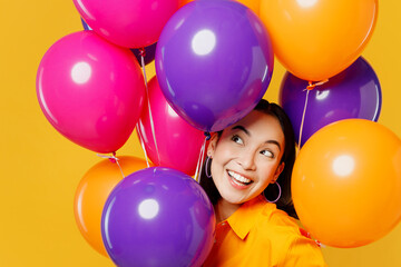 Fototapeta na wymiar Close up happy fun cute amazed young woman in casual clothes celebrating hold look overhead on bunch of colorful air balloons isolated on plain yellow background. Birthday 8 14 holiday party concept