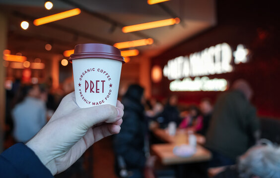 Hand holding a cup of fresh coffee inside a Pret A Manger coffee shop from London, 2023.