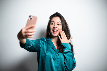 Young brunette attractive girl in casual green silk shirt taking selfie having fun smiling with dimples widely and happily at the camera, blogging