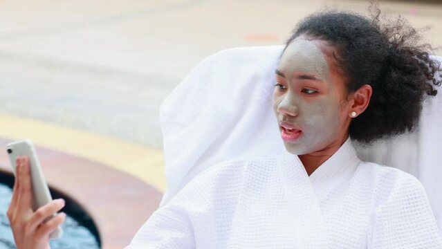 Selfie. Beautiful African American woman holding smart phone in hand shooting selfie photo in beauty spa and wellness center. Facial treatment and skin care concept.