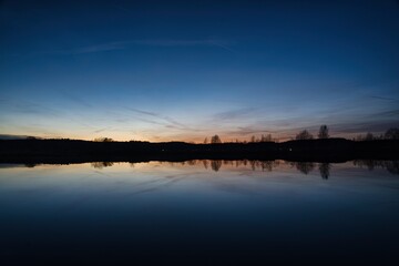 Obraz premium Wonderful blue golden red sky after sunset with trees in foreground at a lake with its reflections 