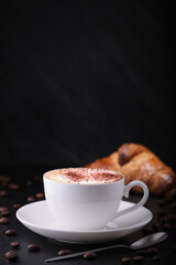 White cup with cappuccino on a black background. Italian breakfast on a black background. Cappuccino, croissant on a black background