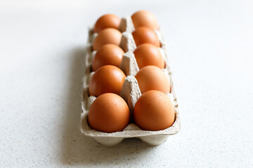a dozen brown farm eggs in a cardboard tray on a light background. proper nutrition, cooking at home.