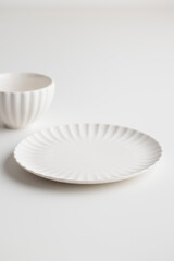 Empty tableware - white plate and a cup on white table as a background for a dessert