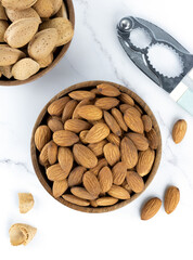 Roasted almonds in a wooden bowl and nutcracker on a marble background. Top view. Selective Focus