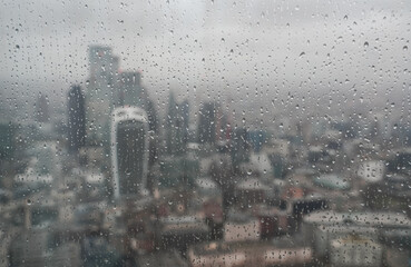 London in cloudy day, drops of rain on the window. Aerial view of London sky scraper buildings and Tower Bridge.