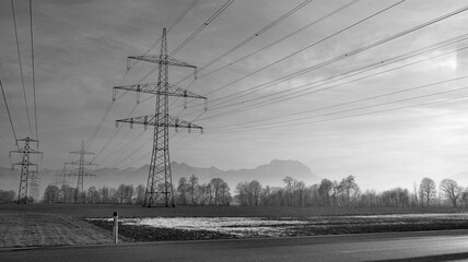 Landscape in winter with many power pylons in background in black and white
