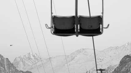 Fototapeta na wymiar 2-seater chairlift with mountains in the background in black and white