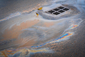Oil slick on the asphalt road background drains into the storm drain.Water pollution environmental...