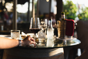 Hand holding glass of red wine in restaurant on table outdoor.
