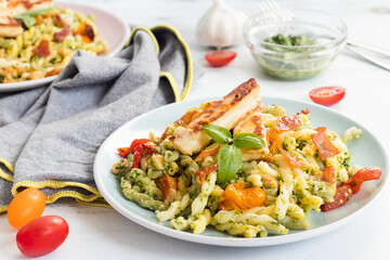 Fusilli pasta with green pesto, baked tomatoes, crunchy ham and grilled cheese served on white plate