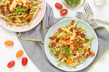 Fresh pasta with green pesto, baked tomatoes, crunchy ham and grilled cheese served on white plate, top view.