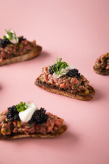 Tatar Canapé vom Rind mit Schmand, Kaviar, Dill als Vorspeisen Fingerfood Häppchen auf rosa pink Hintergrund