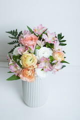 Beautiful bouquet of fresh colorful pastel ranunculus and lily flowers in full bloom with green fern leaves in vase against white background. Spring bunch of buttercups.