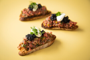 Tatar Canapé vom Rind mit Schmand, Kaviar, Dill als Vorspeisen Fingerfood Häppchen auf pastell gelb Hintergrund