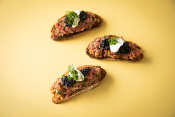 Tatar Canapé vom Rind mit Schmand, Kaviar, Dill als Vorspeisen Fingerfood Häppchen auf pastell gelb Hintergrund