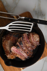 Entrecote Steak vom Rind medium rare gebraten in Gusseisen Pfanne mit Meersalz auf Holzbrett mit Messer, Fleischgabel und hellen Marmor Hintergrund