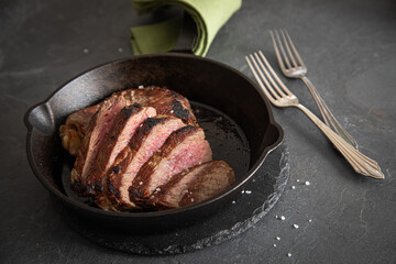 Entrecote Steak vom Rind medium rare gebraten in Gusseisen Pfanne mit Meersalz auf schwarzen Schiefer mit Gabel, grünen Tuch und dunklen Stein Hintergrund