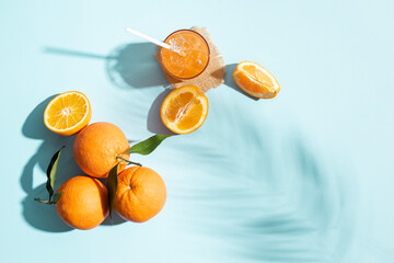Orange fruit top view with slice and glass of juice on blue background with sunlight.