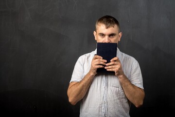 a man of European appearance holds a book in his hands in front of his face. place for text