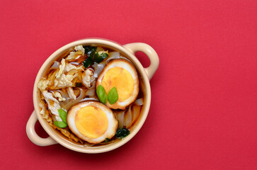 Appetizing Asian soup with noodles, Chinese cabbage and eggs in a bowl on a red background