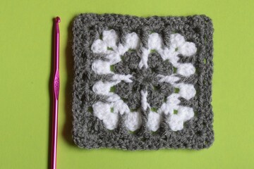 Modern Crochet granny square in grey and white with crochet hook isolated on a plain green background with copy space - 558679167