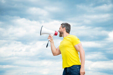 man in yellow shirt screaming in loudspeaker on sky background