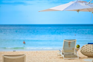 White sand beach and blue sea landscape view of a tropical resort hotel beside modern swimming pool, white parasols, palm trees, deck beach chairs in the golden sunset time