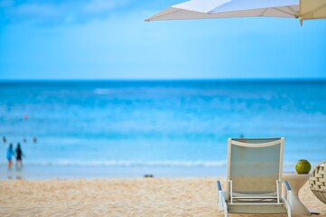 White sand beach and blue sea landscape view of a tropical resort hotel beside modern swimming pool, white parasols, palm trees, deck beach chairs in the golden sunset time