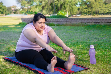 Overweight indian woman doing stretching exercise outdoors in park while watching online training...