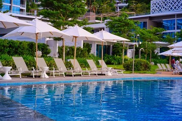 White sand beach and blue sea landscape view of a tropical resort hotel beside modern swimming pool, white parasols, palm trees, deck beach chairs in the golden sunset time