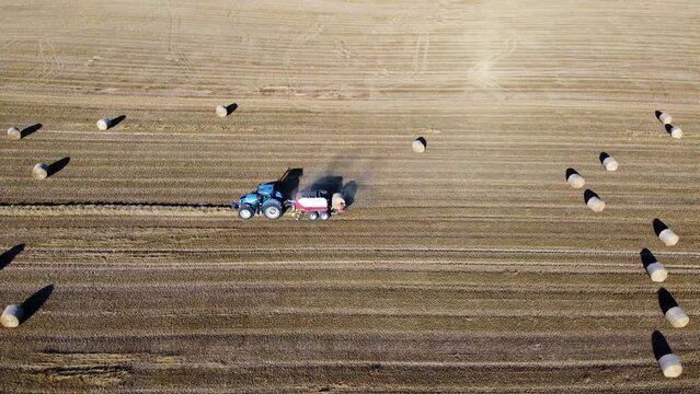 Tracteur en train de faire des bottes de foin. Vue de profil avec le tracteur munis de sa presse &agrave; foin qui fait tomber une boule.