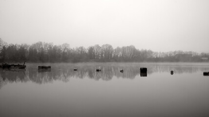 Industrial canister floating on the lake with reflections of trees in the water in black and white
