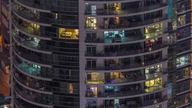 Light in windows of modern towers. Exterior of apartment building at night with glowing windows timelapse. Aerial view of skyscraper with illumination from above. Cars parked behind