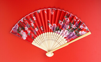 Red Oriental Chinese fan with a flower pattern closeup. Isolate on red background. Top view.