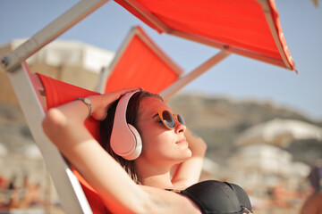young woman lying on a sunbed at the beach listens to music