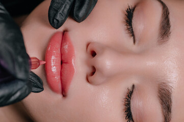 Permanent lip makeup. The cosmetologist makes the procedure of permanent makeup to the client in...